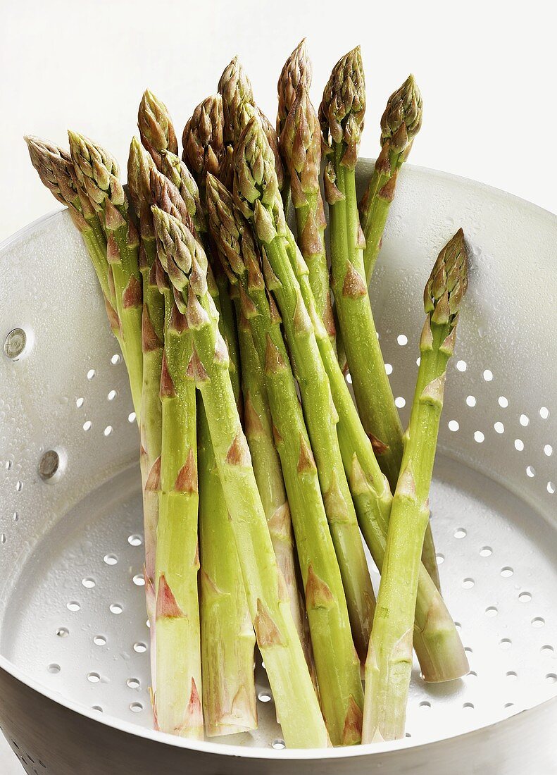 Several spears of green asparagus in a metal colander