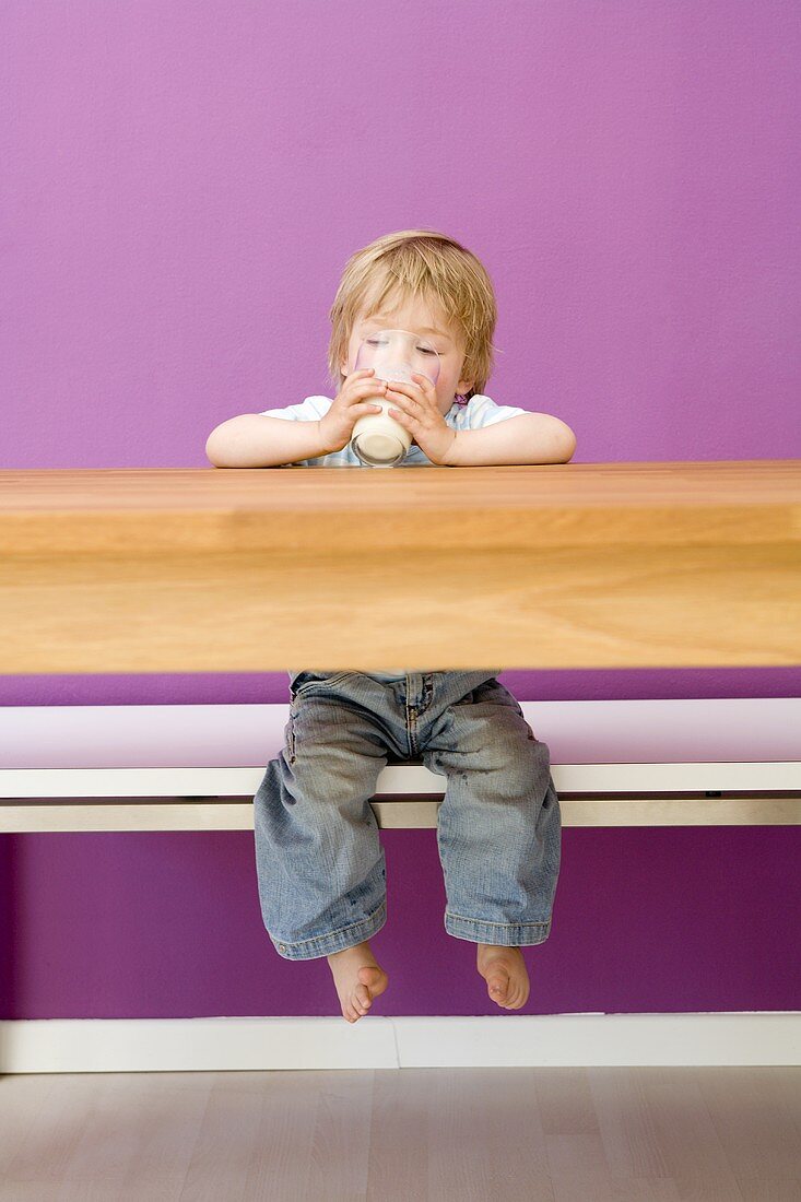 Small boy drinking milk at wooden table