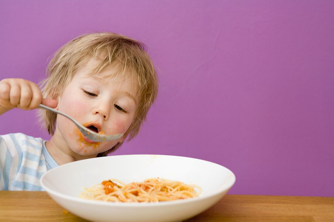 Small boy eating spaghetti with tomato sauce