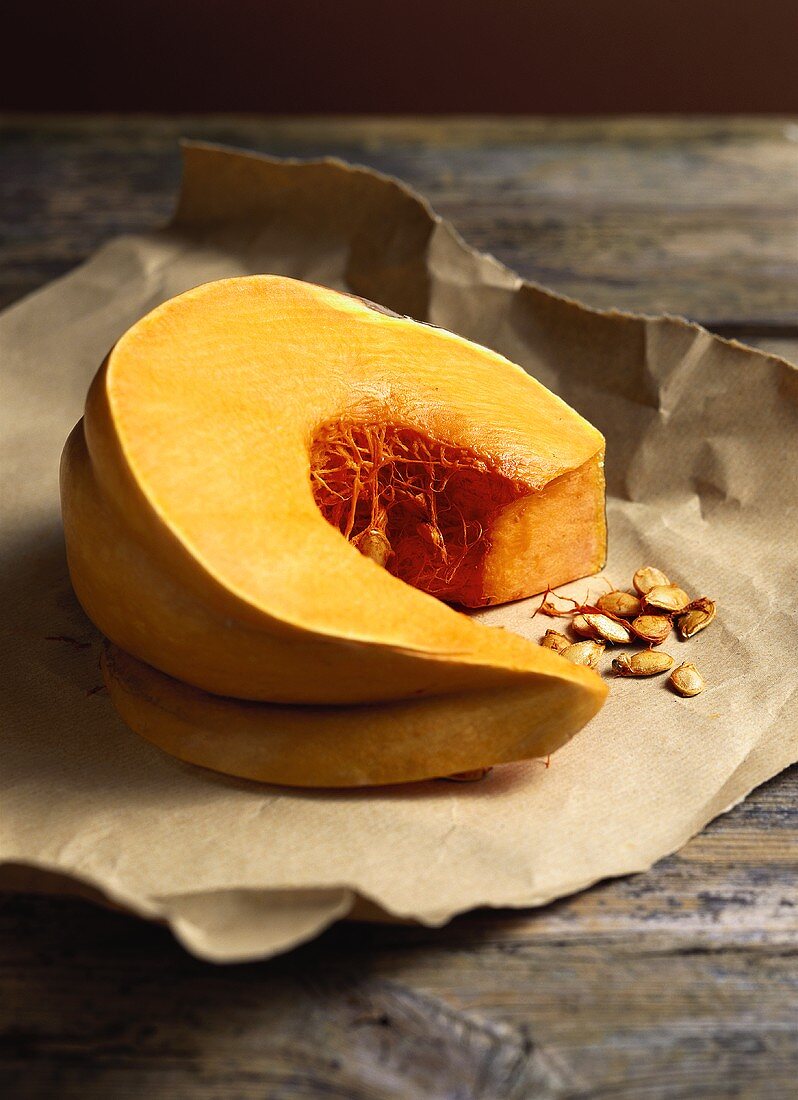 Wedge of pumpkin and pumpkin seeds on brown paper