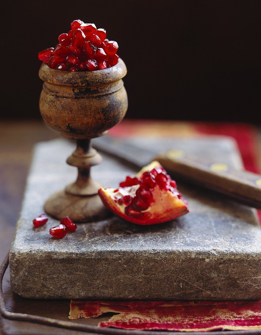 Pomegranate seeds in container, piece of pomegranate beside it