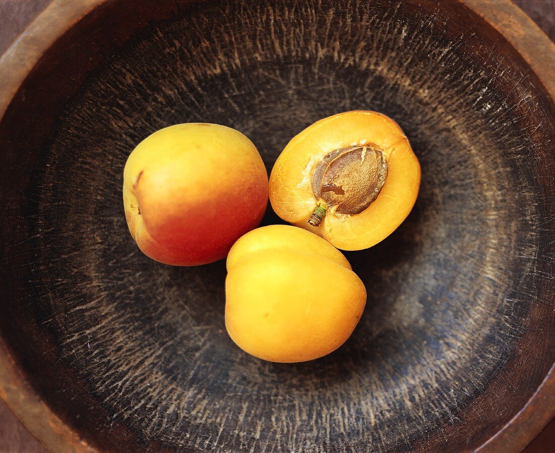 Two whole apricots and half an apricot on brown plate