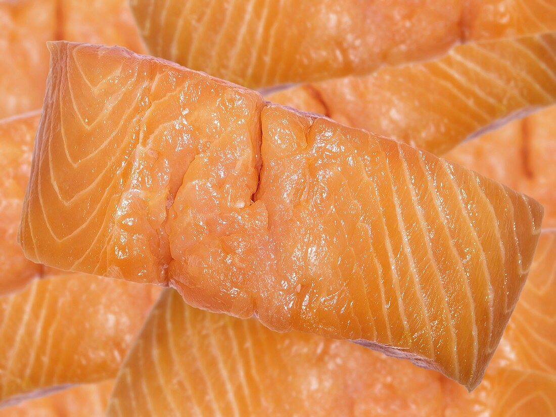 A salmon fillet with lots of salmon fillets in background