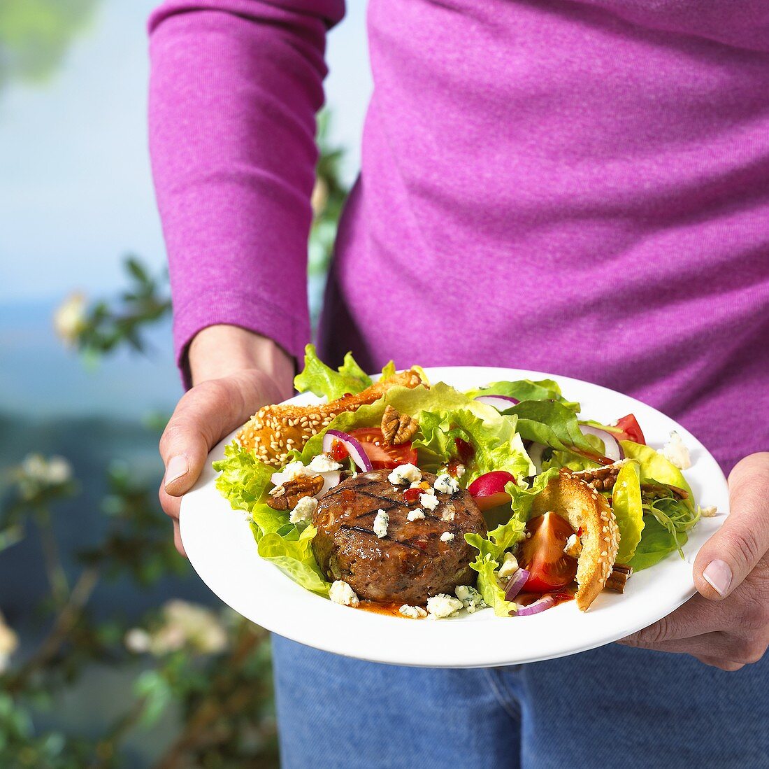 Zwei Hände halten Teller mit Burger-Salat