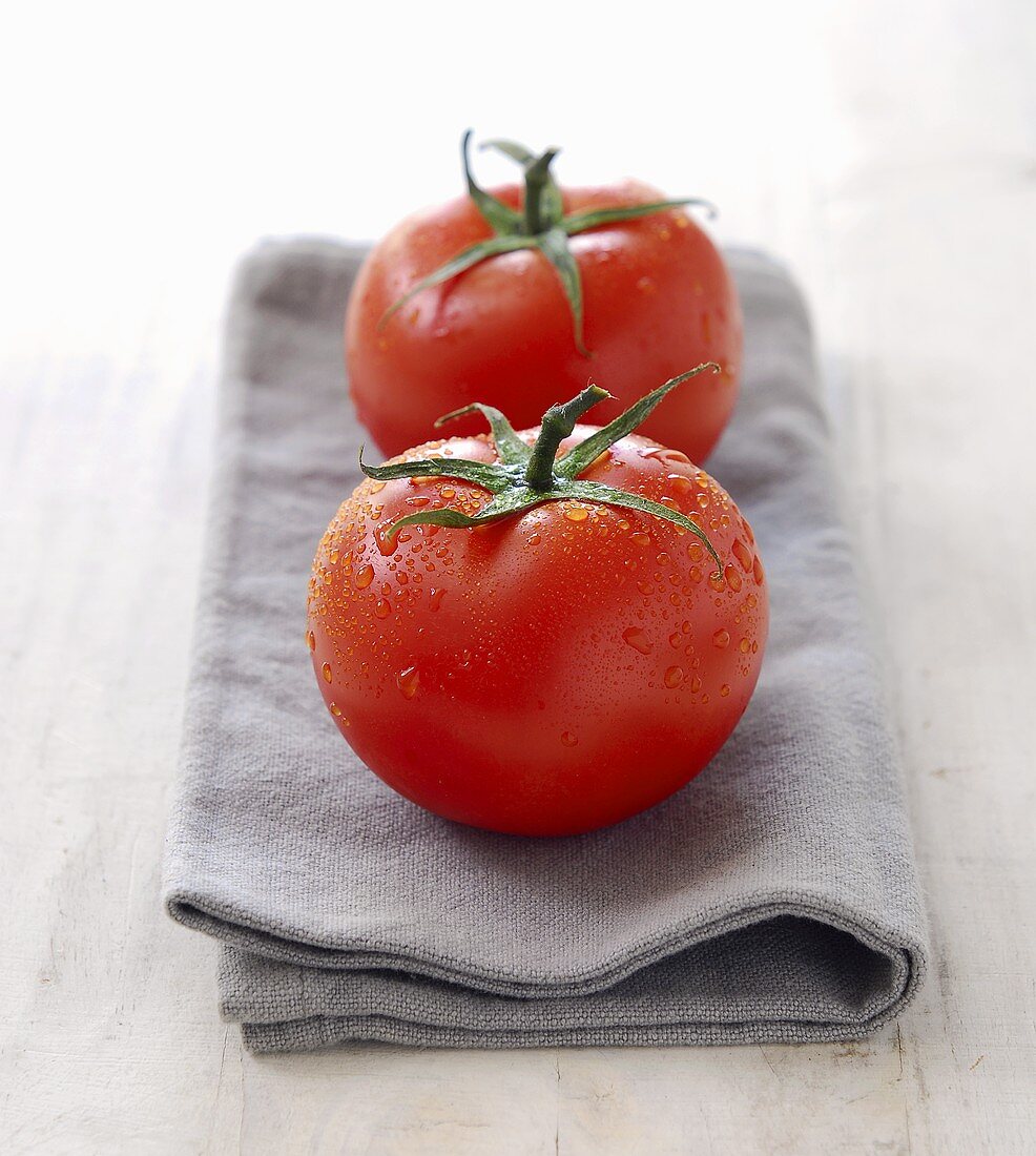 Two tomatoes with drops of water on napkin