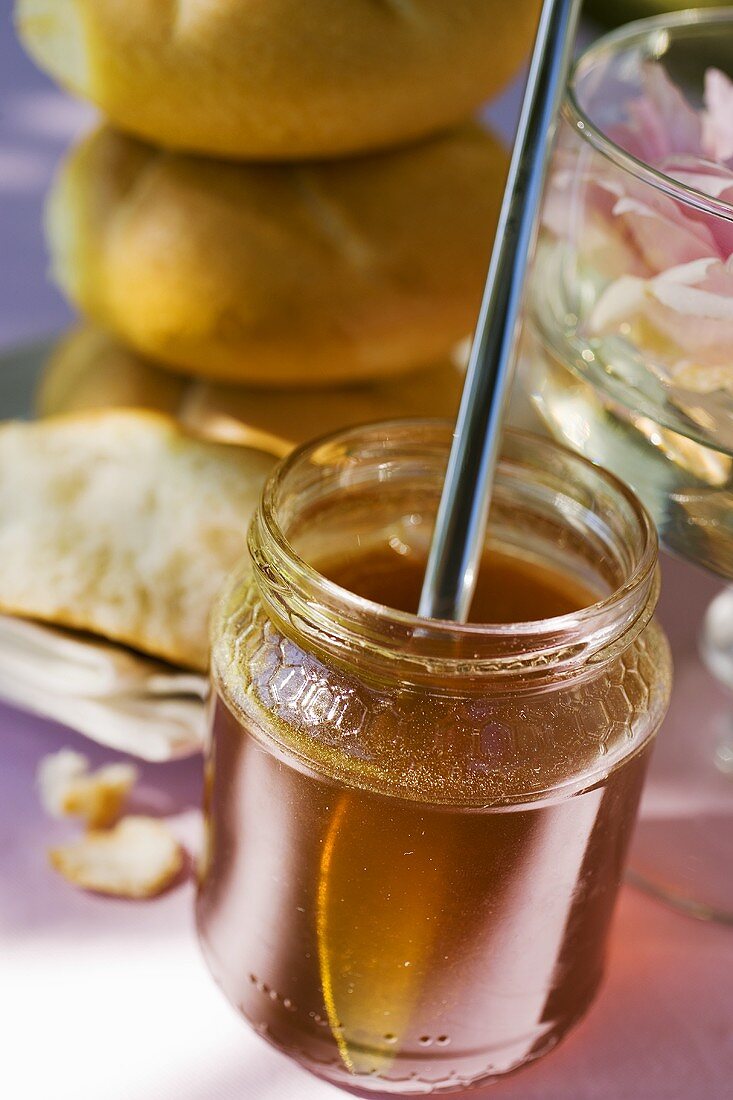Honey in jar, bread rolls behind