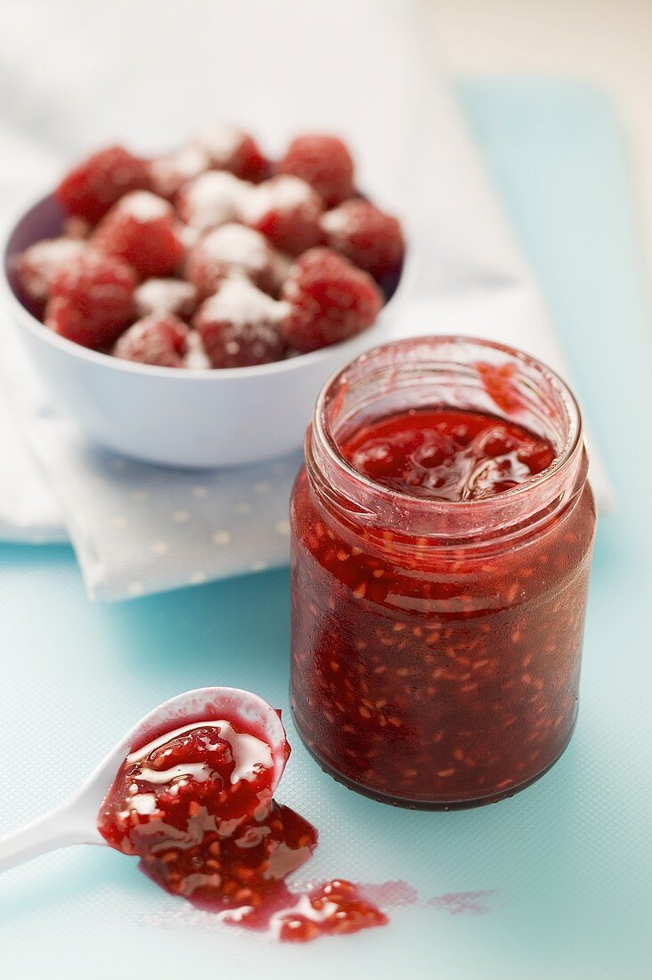 A bowl of strawberries with sugar and strawberry jam in a jar and on a spoon