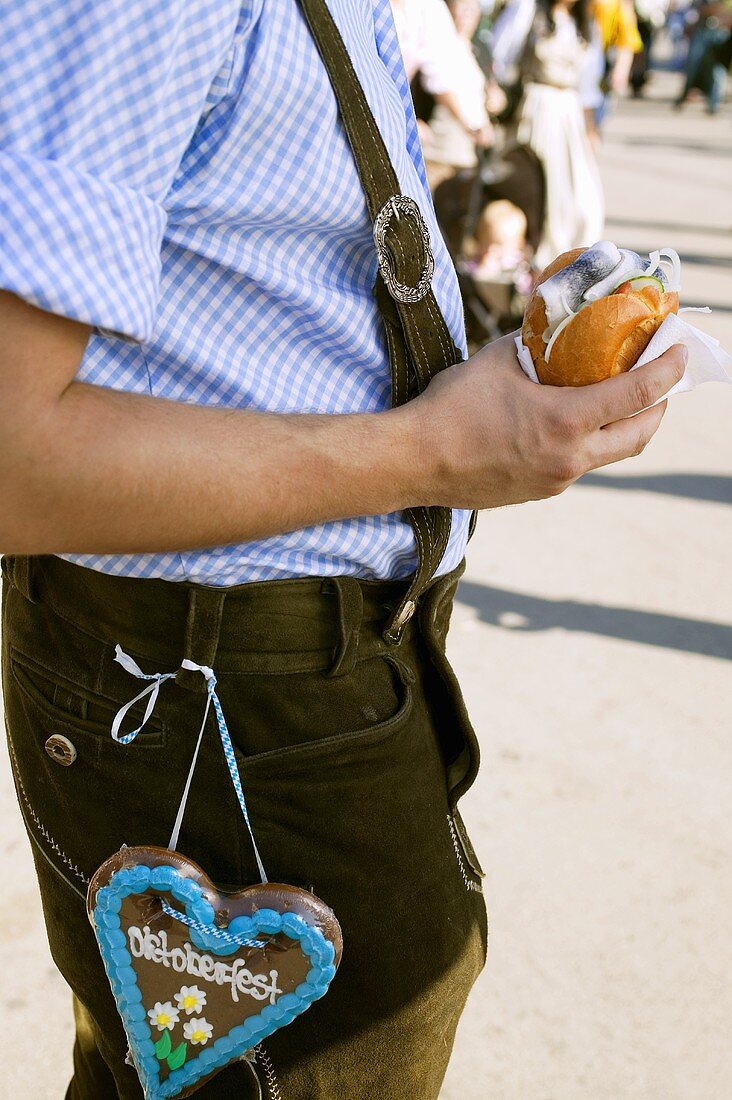 Mann in Tracht hält Heringsbrötchen (München, Oktoberfest)