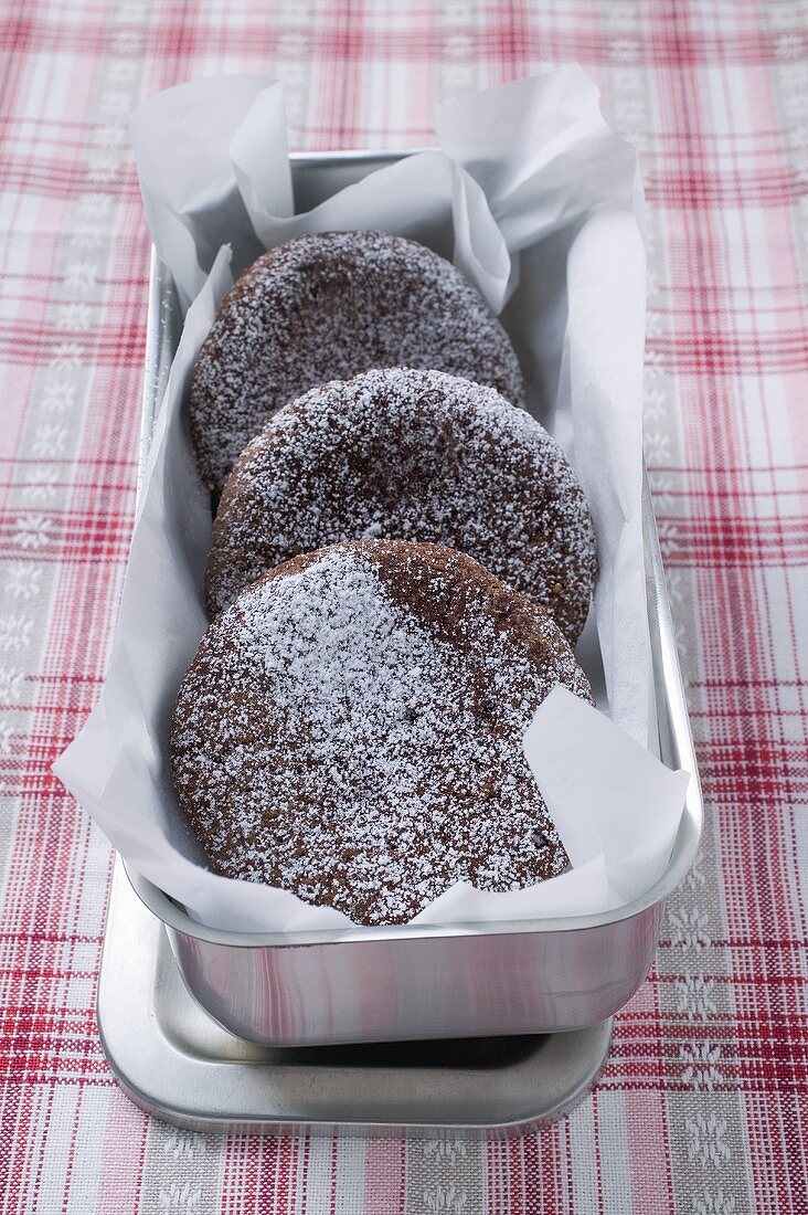 Three chocolate buns with icing sugar