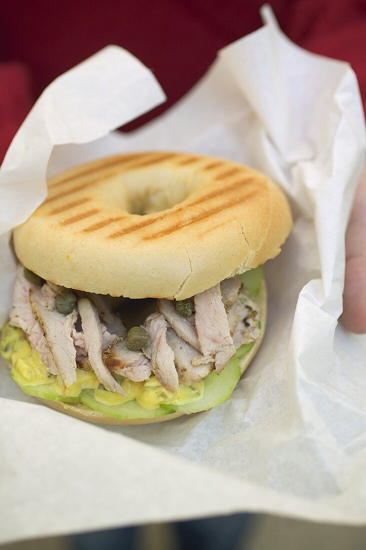 Hände halten Bagel mit Schweinefilet, Kapern und Senfrelish