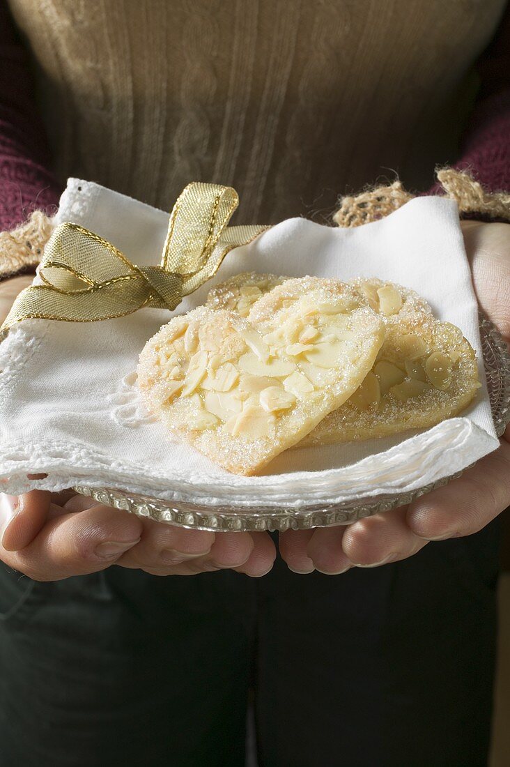 Hands holding almond biscuits on glass plate