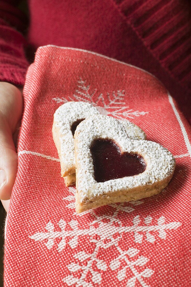 A hand holding jam biscuits in a Christmassy cloth