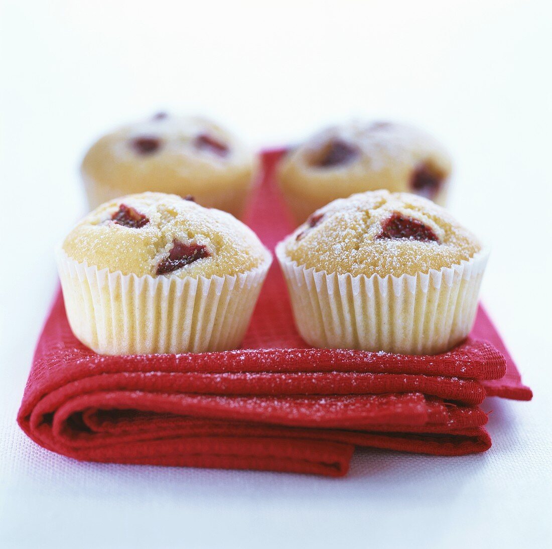 Four muffins in paper cases on red cloth