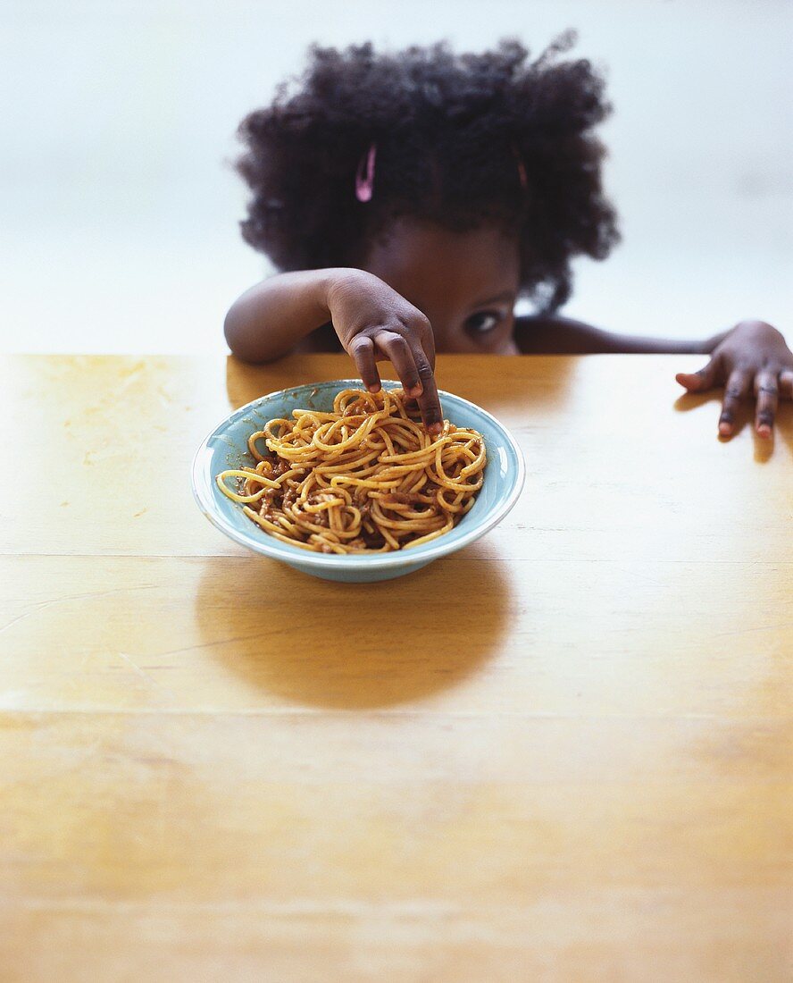 Small girl reaching for spaghetti bolognese