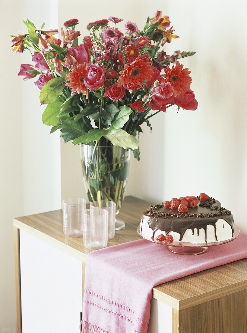 Chocolate cake with cream & raspberries beside vase of flowers