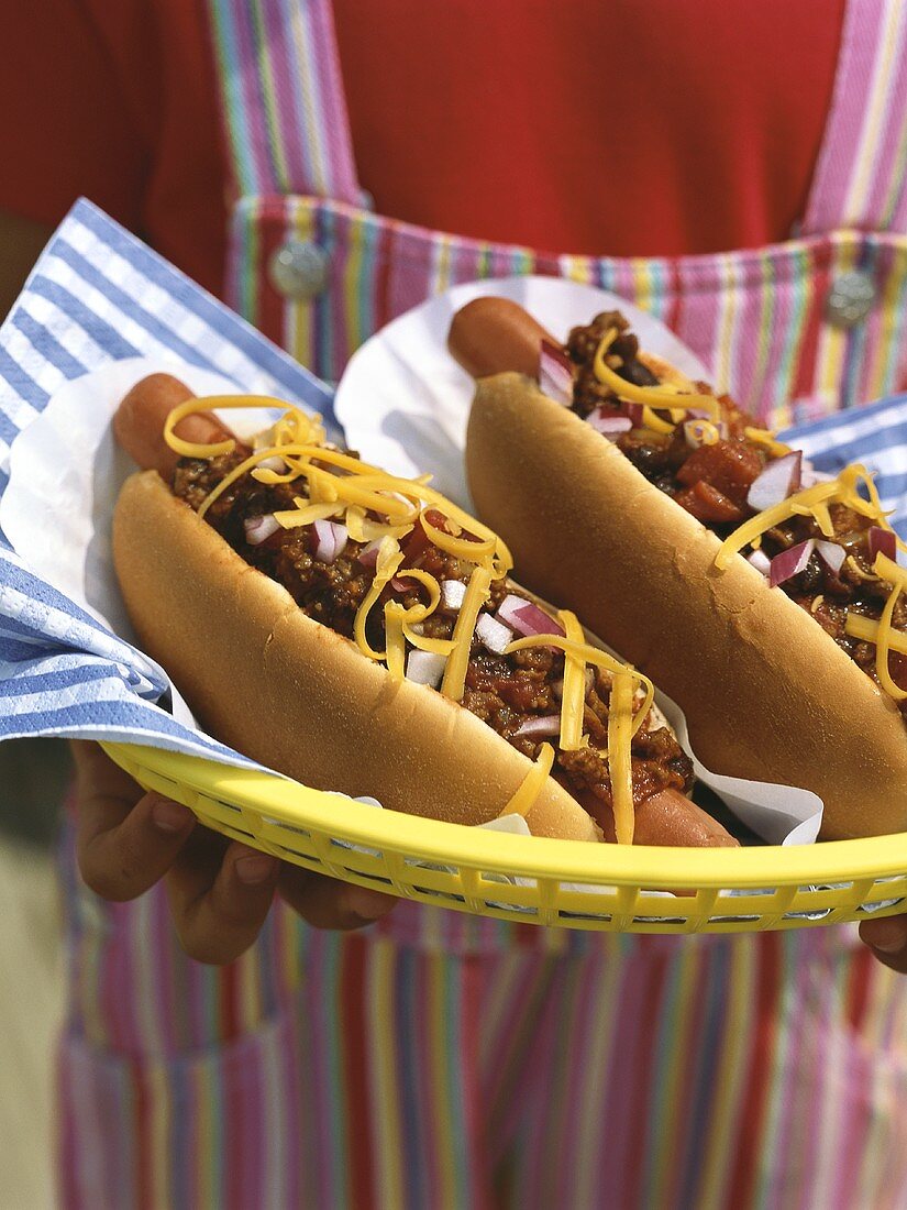 Hands holding two hot dogs with mince sauce and cheese