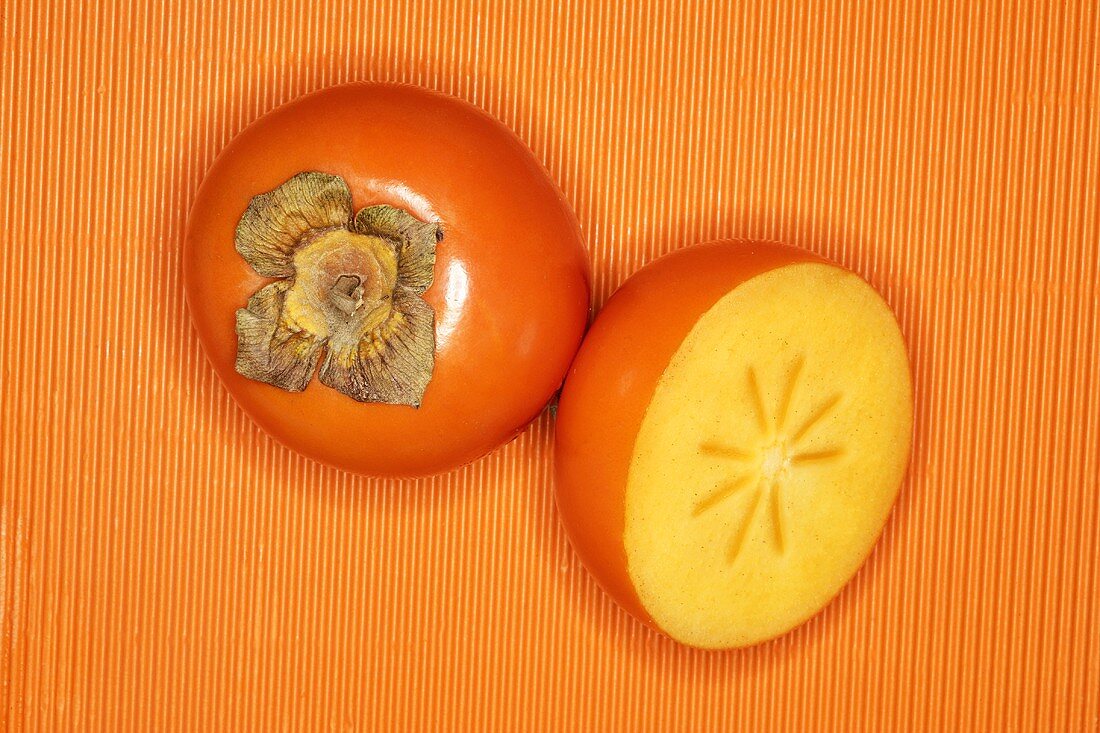 Sharon fruits, whole and half, on orange background