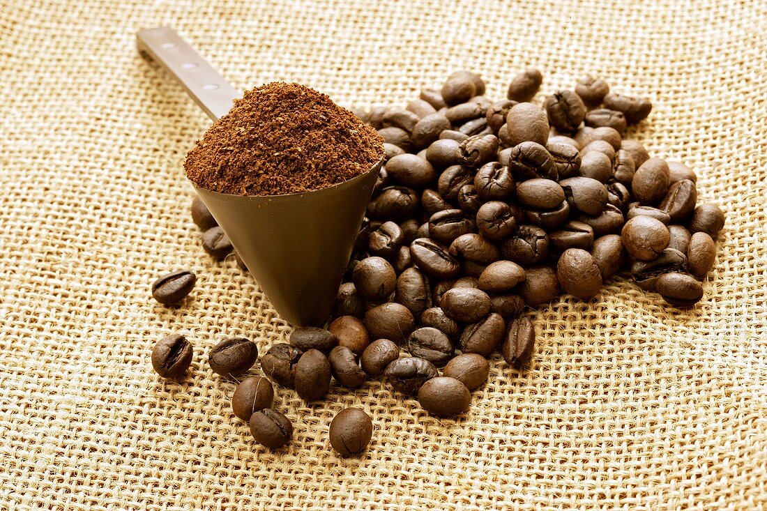 Kaffeepulver im Messlöffel und Kaffeebohnen auf Jute