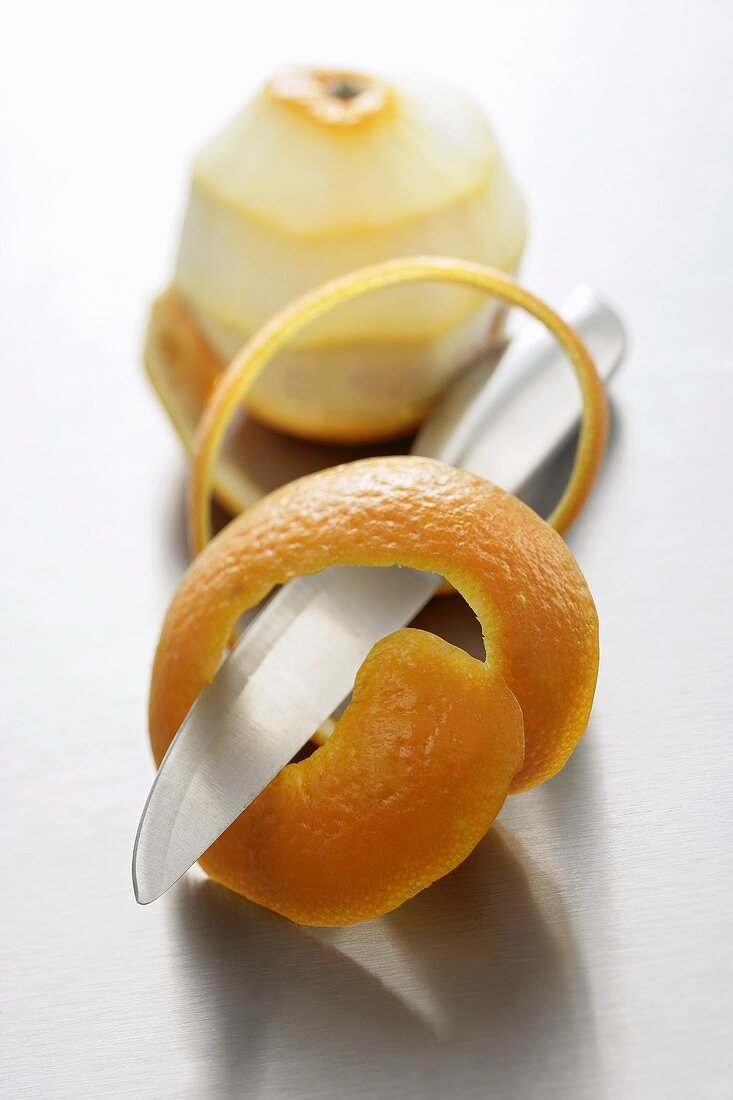 Spiralförmige Orangenschale mit Messer vor geschälter Orange