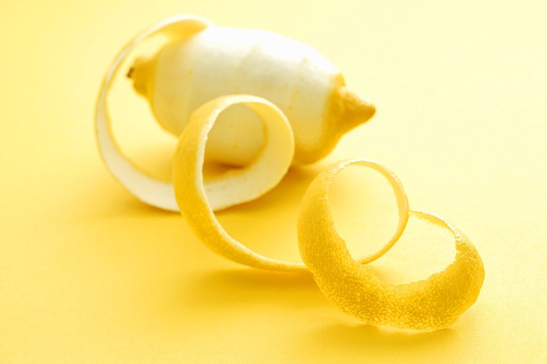 Spiral of lemon peel in front of peeled lemon