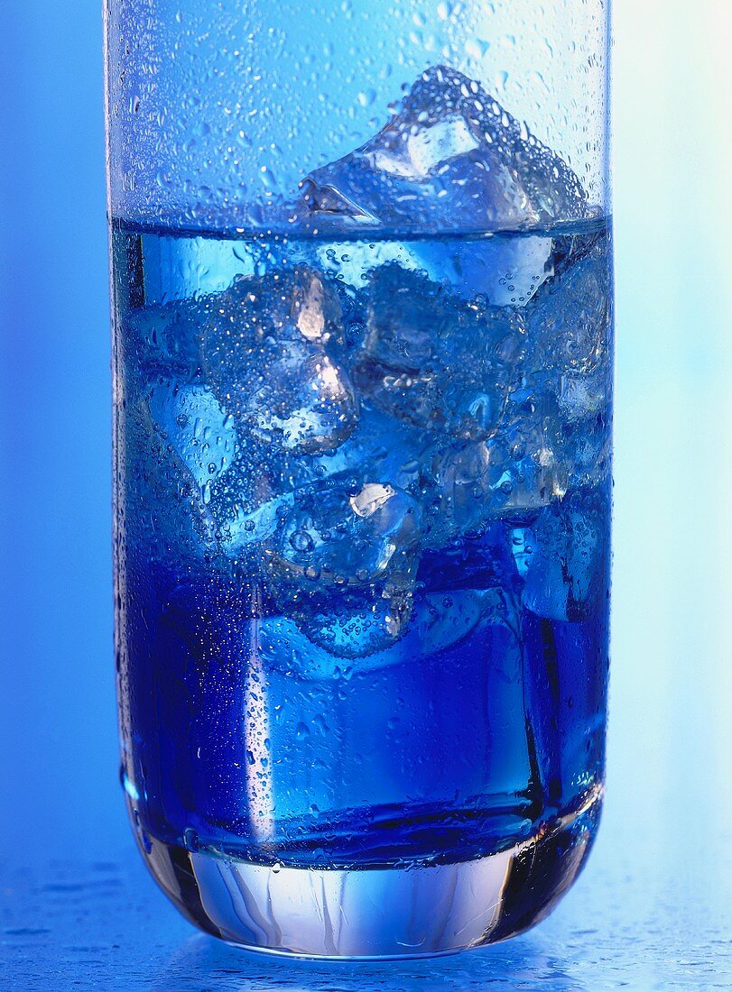 Wasserglas mit Eiswürfeln vor blauem Hintergrund