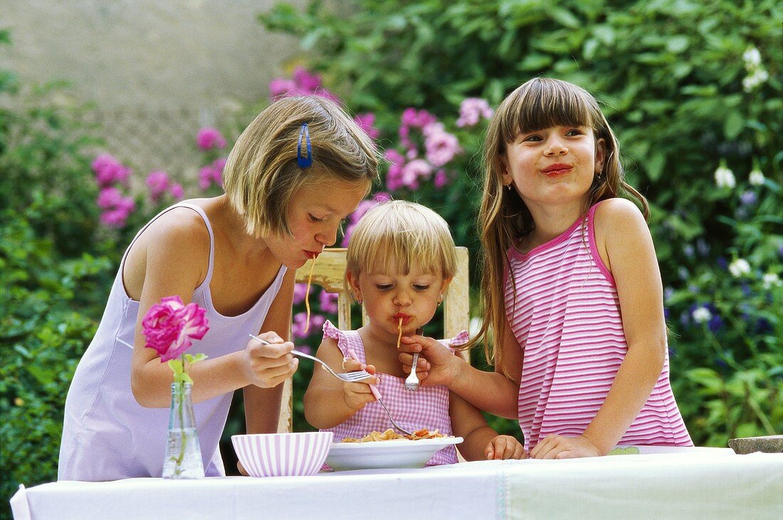 Drei Mädchen essen Spaghetti im Freien
