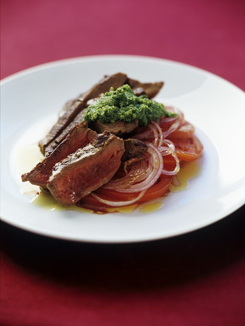 Rump steak with pesto on onions and tomatoes