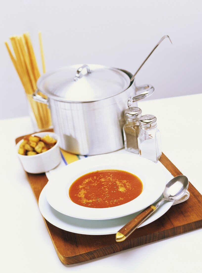 Tomatensuppe, dahinter Croûtons, Kochtopf und Grissini