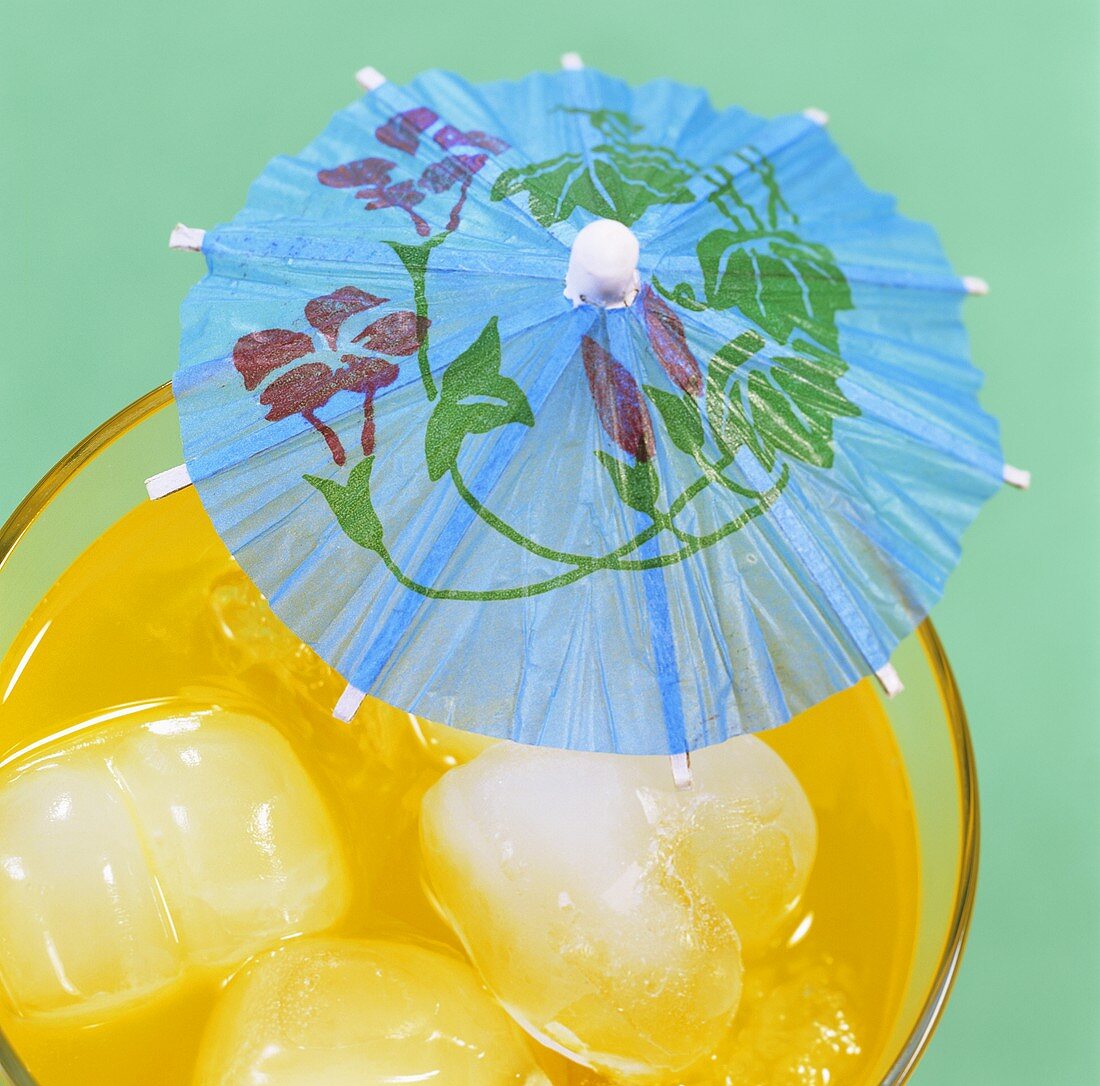 Orange drink with ice cubes and cocktail umbrella