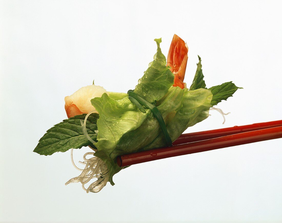 Lettuce leaf with shrimp and rice noodles on chopsticks