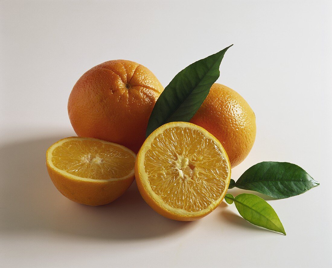 Orangenhälften und ganze Orangen mit Blättern