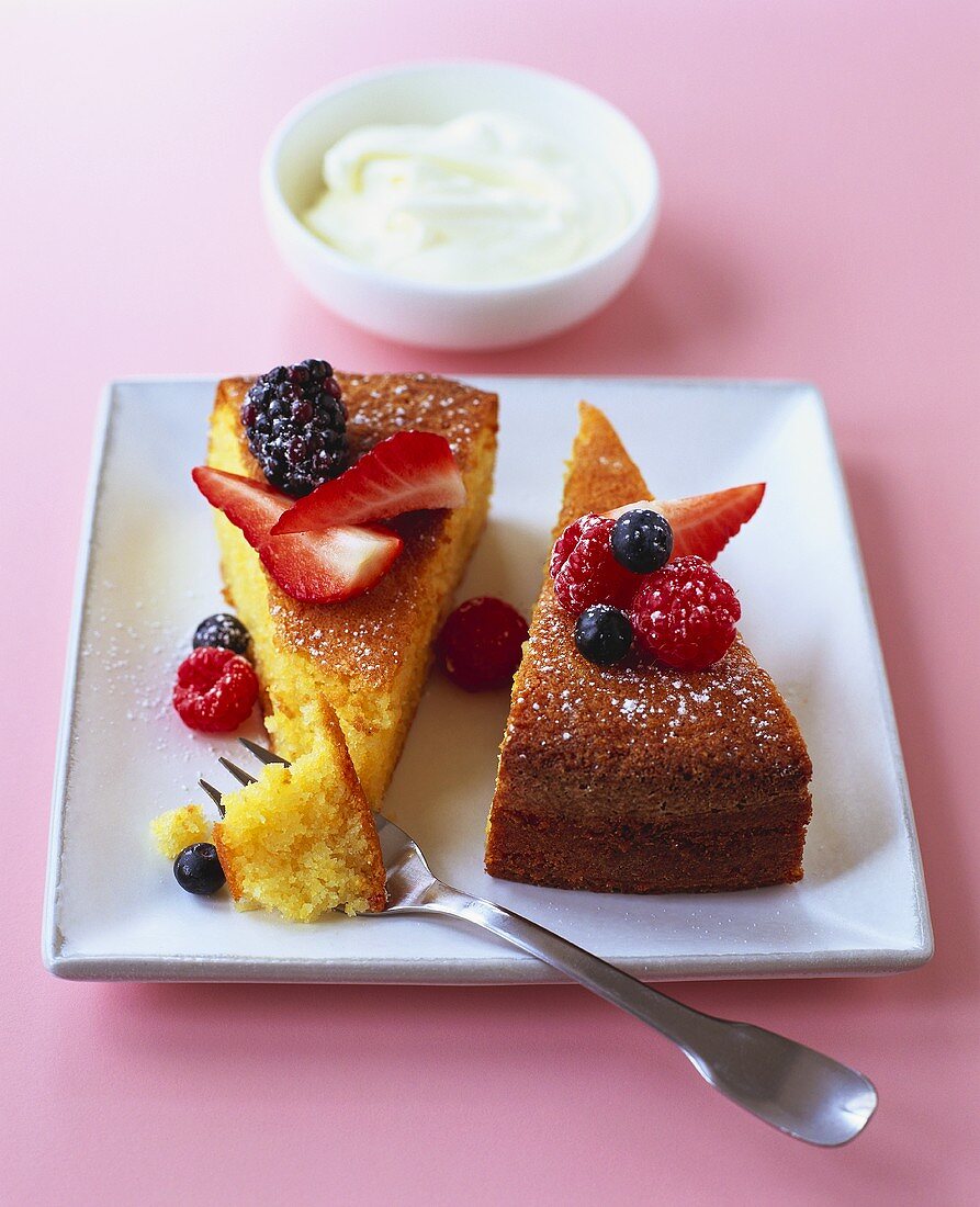 Two pieces of polenta cake with berries and whipped cream