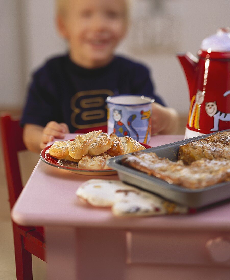 Kleiner Junge am Tisch mit Kuchen, Gebäck und Tasse