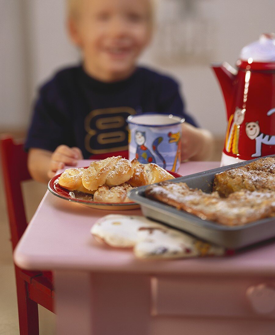 Small boy at table with cakes, pastries and cup