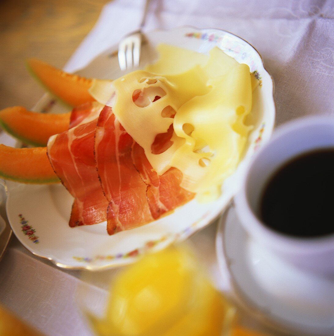 Breakfast of melon, bacon, cheese, coffee and orange juice