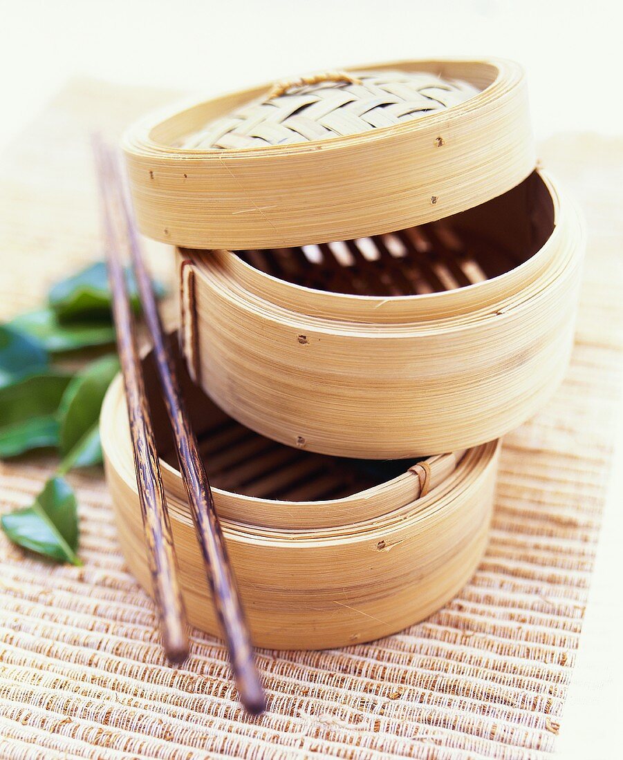 Two steaming baskets and chopsticks on bamboo mat