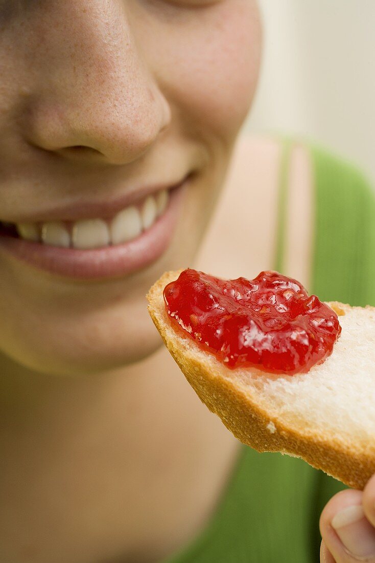 Woman eating a slice of white bread with strawberry jam