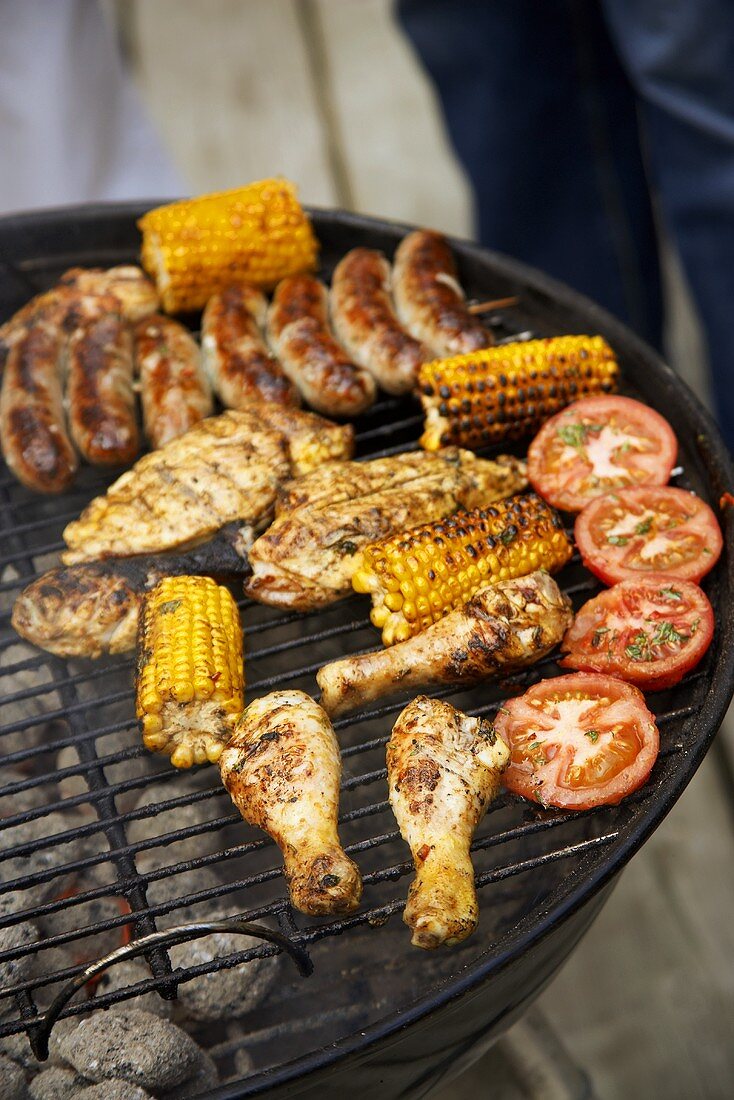 Chicken pieces, corncobs, tomatoes & sausages on a barbecue