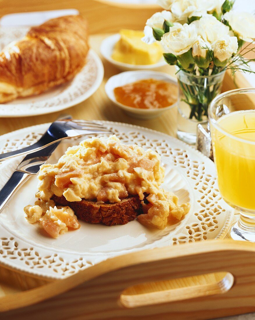 Frühstückstablett mit Rührei, Saft, Croissant und Marmelade