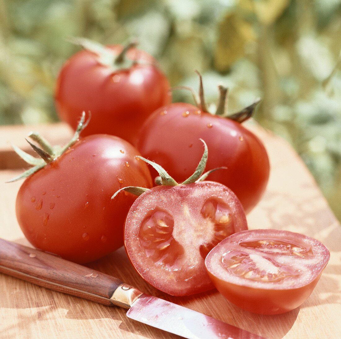 Fresh tomatoes with knife on wooden board