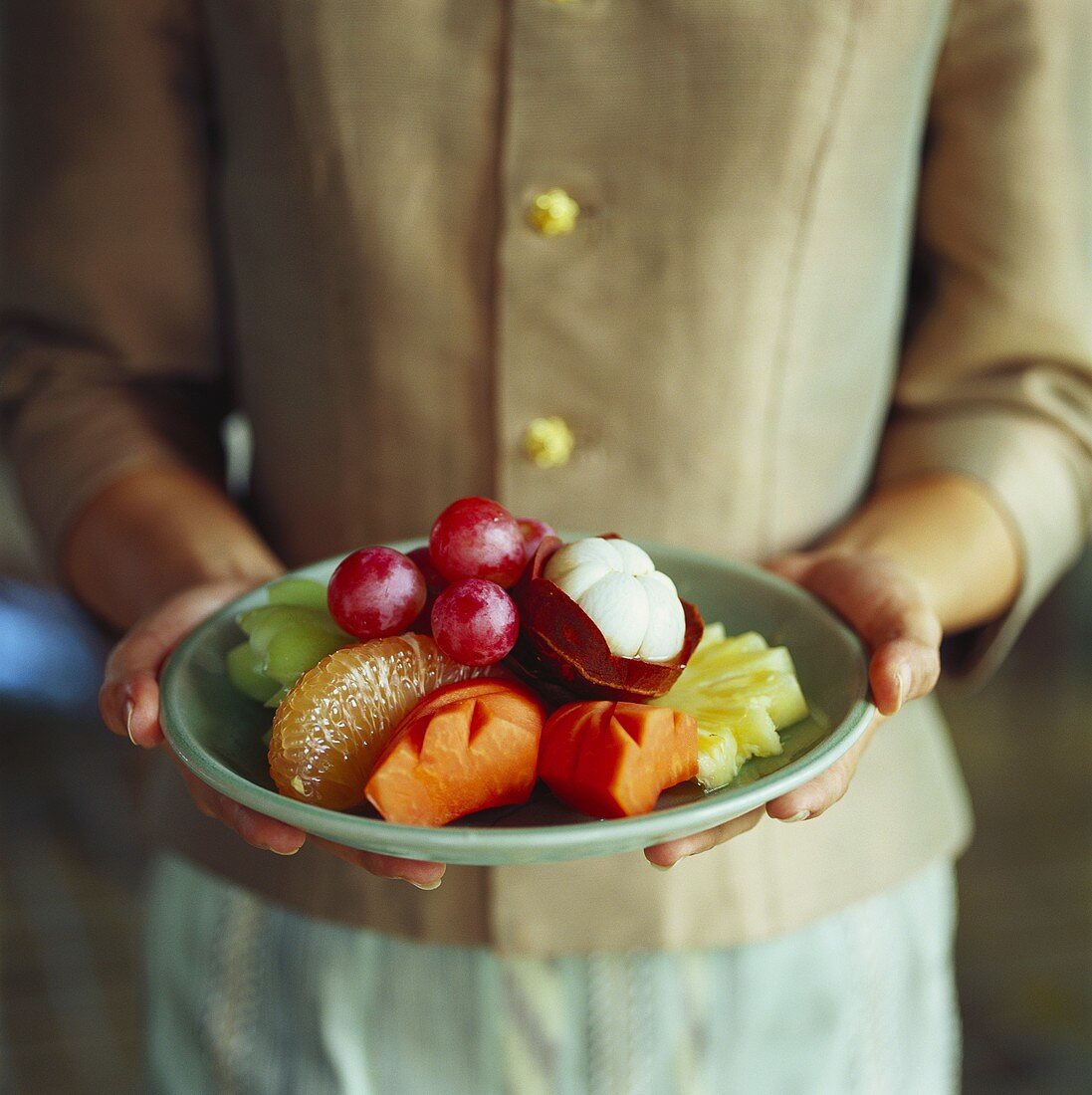 Hände halten einen Teller mit Südfrüchten