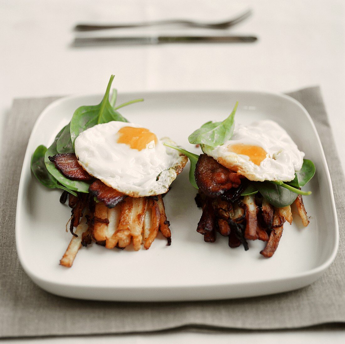 Fried egg with bacon and spinach on potato sticks