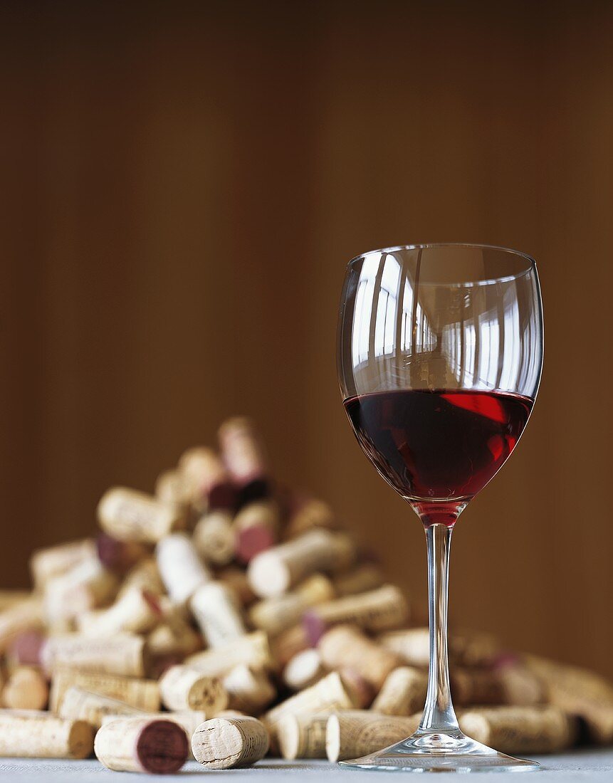 A glass of red wine and lots of corks