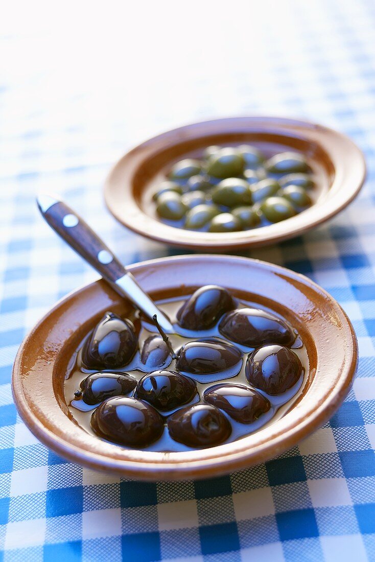 Black and green olives in small bowls on checked cover