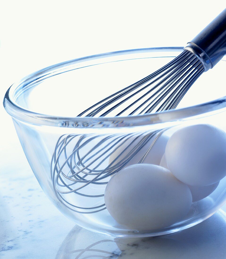 weiße Eier und ein Schneebesen in einer Glasschüssel