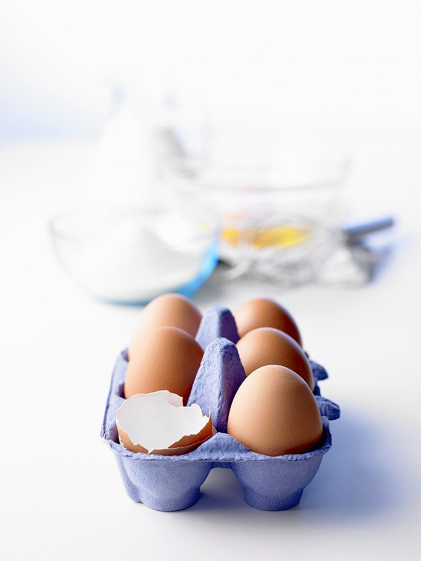 Egg box with brown eggs, baking ingredients behind