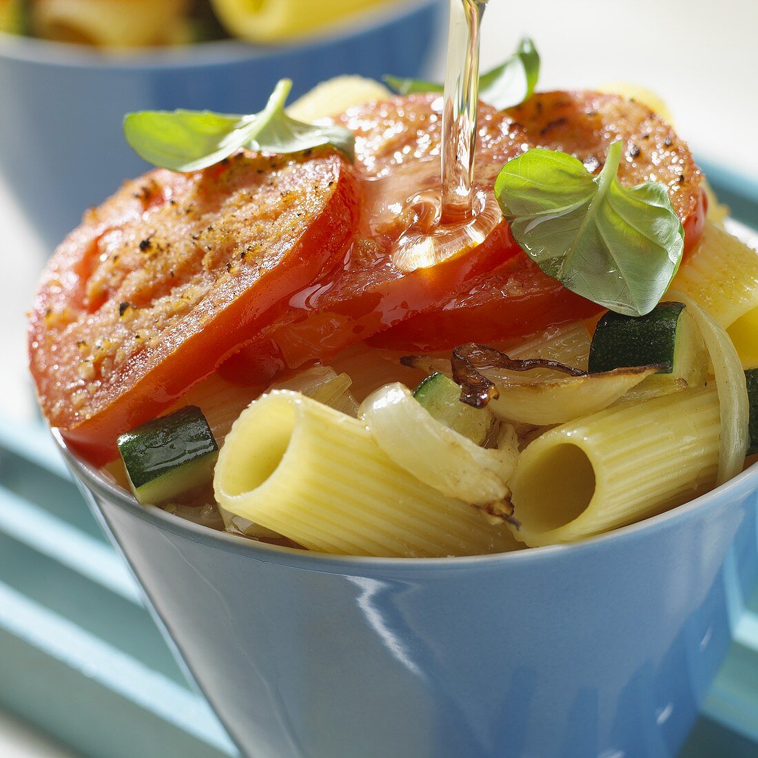 Olive oil being poured over tortiglioni and tomatoes 