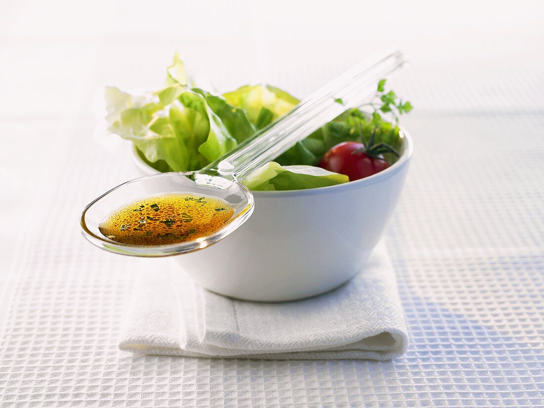 Spoonful of salad dressing lying on a bowl of salad