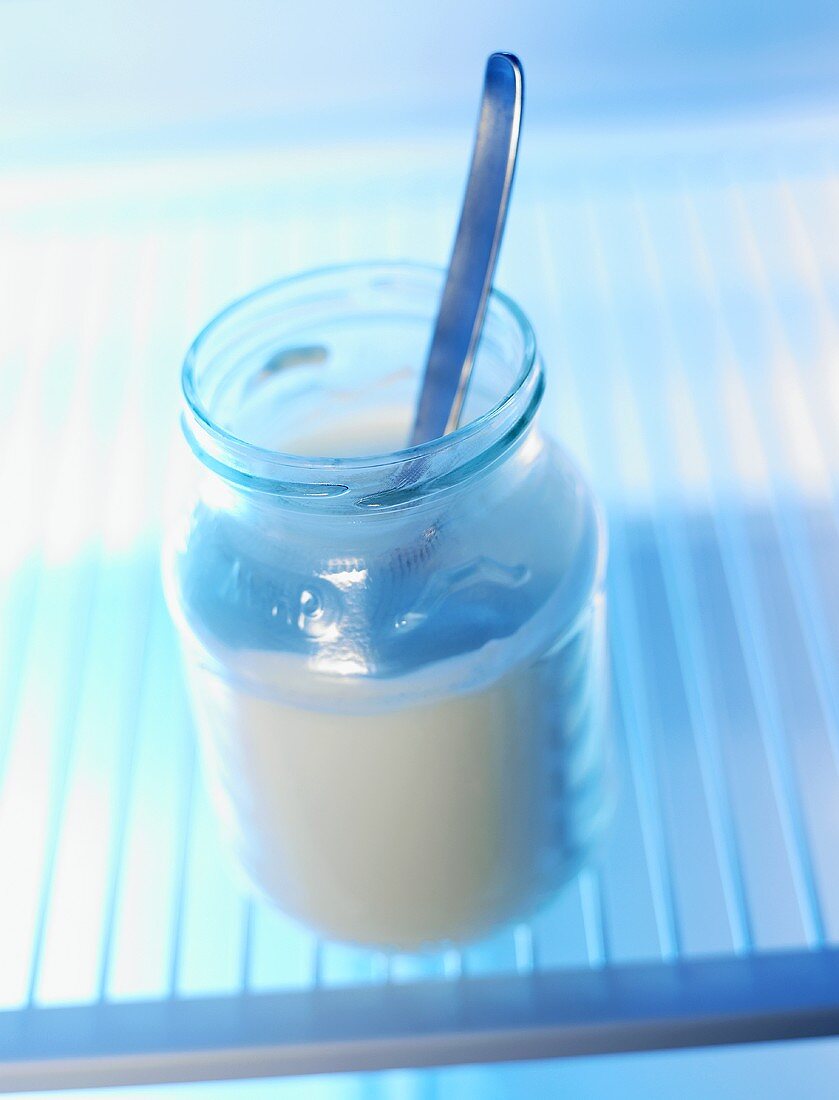 Geöffnetes Joghurtglas mit Löffel im Kühlschrank