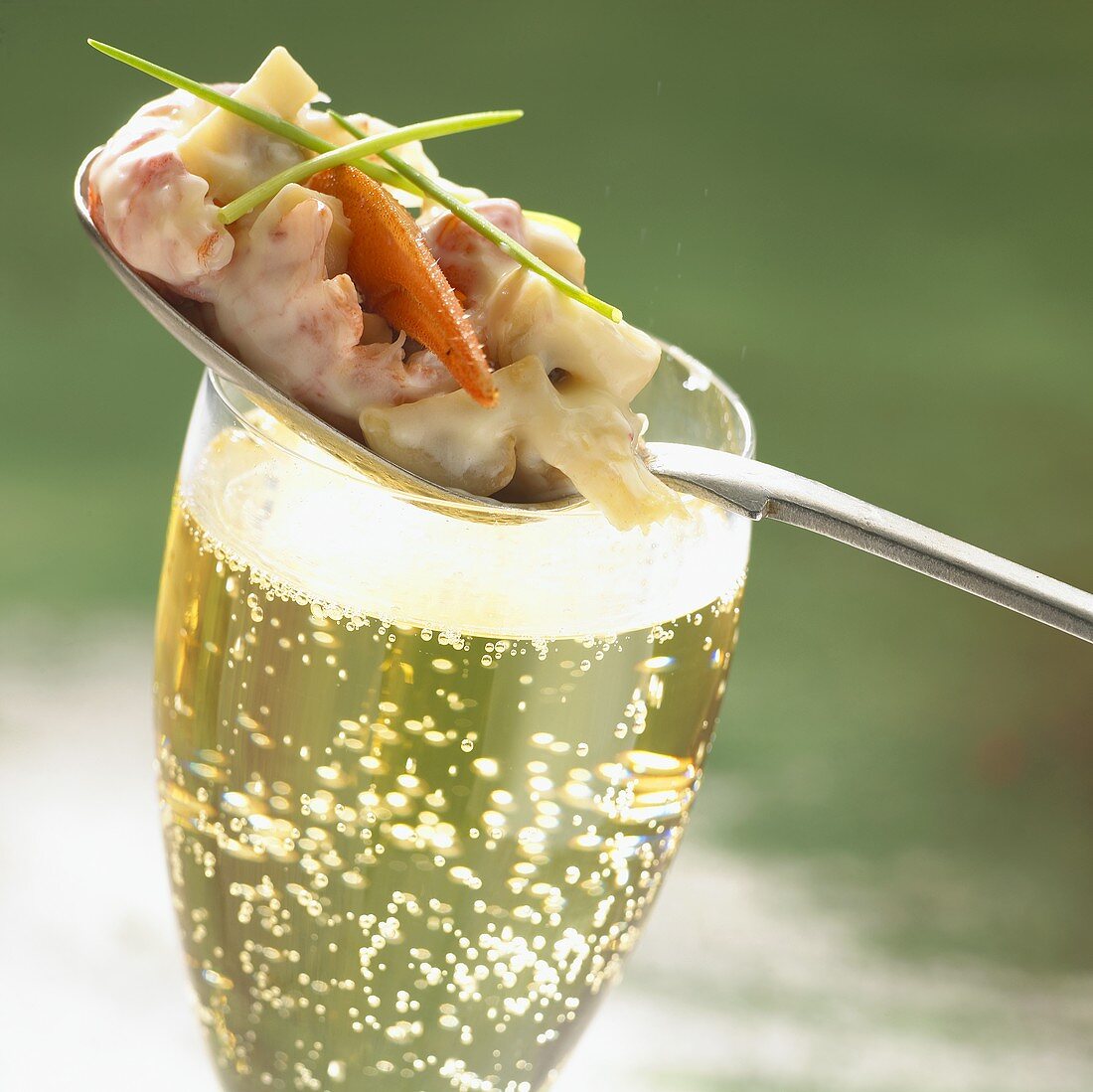Krabbencocktail auf einem Löffel, dazu ein Glas Champagner